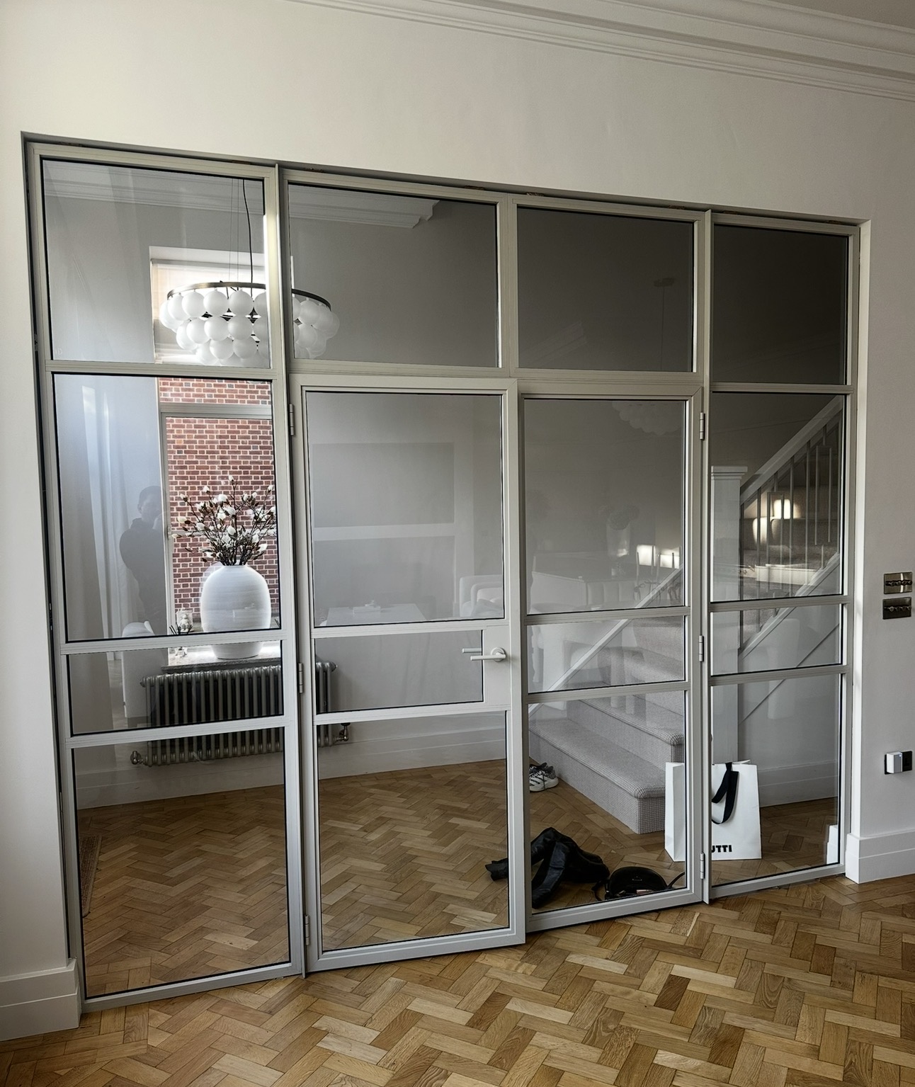 Silver aluminium glazed screen with hinged door dividing a hallway and dining room